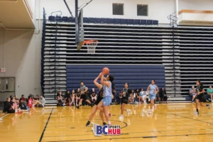 An athlete from Showtime Basketball tries for a layup while in close contact with the defender from Raise Her Game.