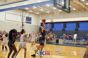 #12 from New West Elite attempts a layup while her defender loses balance and falls backwards.
